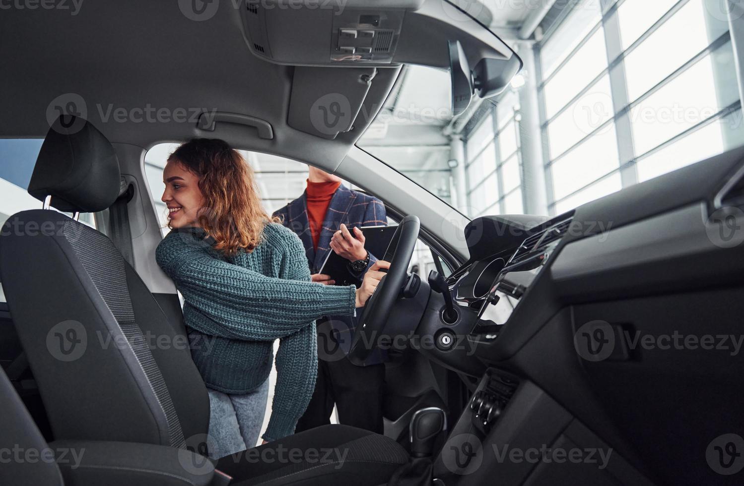 Professional salesman assisting young girl by choosing new modern automobile indoors. Woman sitting inside photo