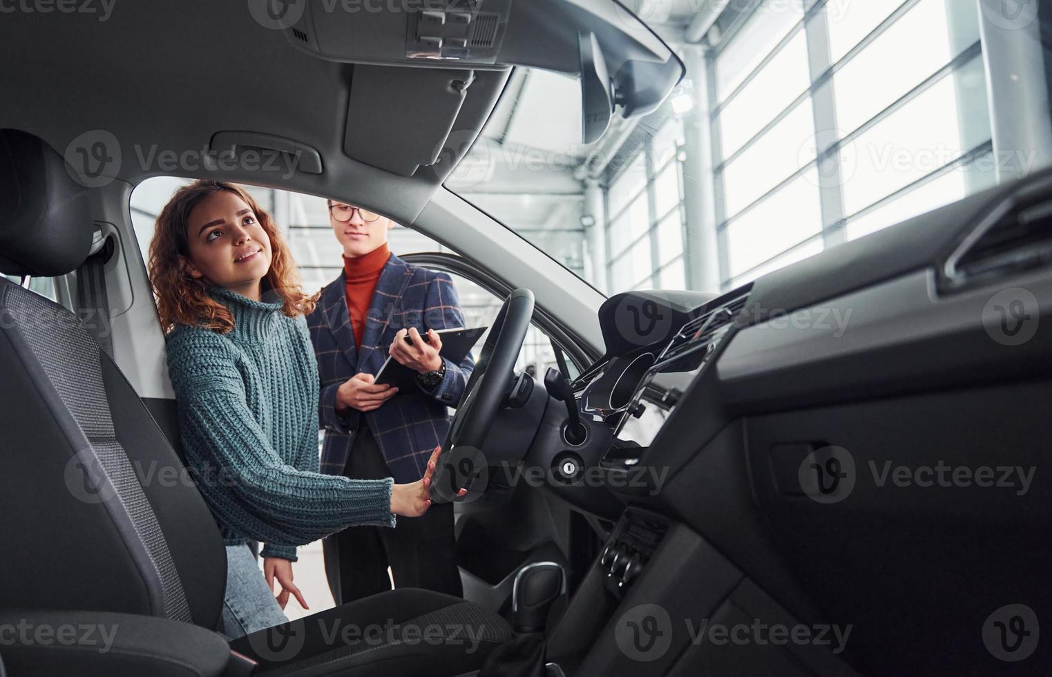 Professional salesman assisting young girl by choosing new modern automobile indoors photo