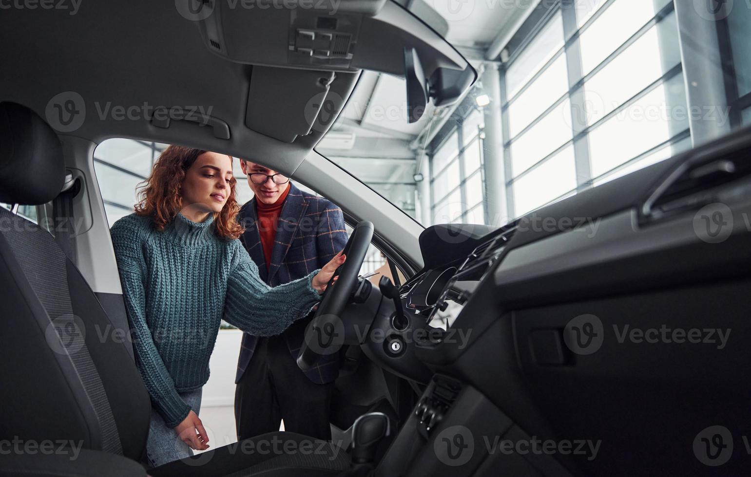 Professional salesman assisting young girl by choosing new modern automobile indoors. Woman sitting inside photo