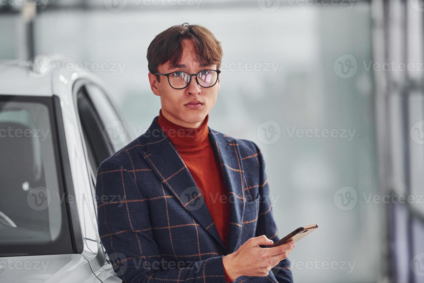 Hipster in formal wear and in eyewear standing near white modern car indoors photo
