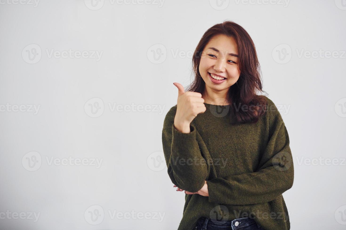 Portrait of happy asian young girl that shows thumb up indoors in the studio against white background photo