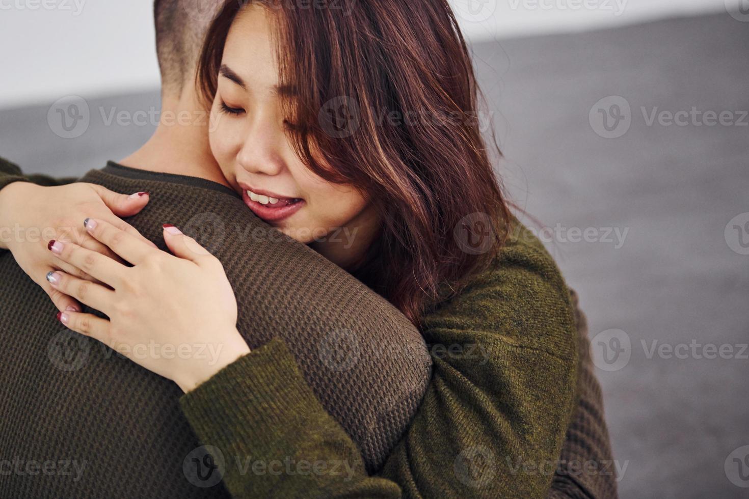 Happy multi ethnic couple in casual clothes sitting together indoors in the studio. Caucasian guy with asian girlfriend photo