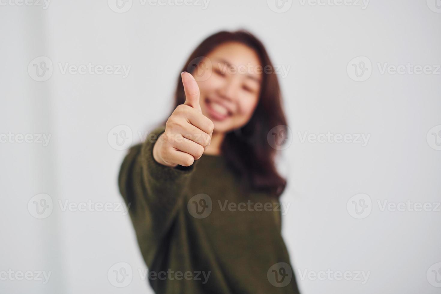 Portrait of happy asian young girl that shows thumb up indoors in the studio against white background photo