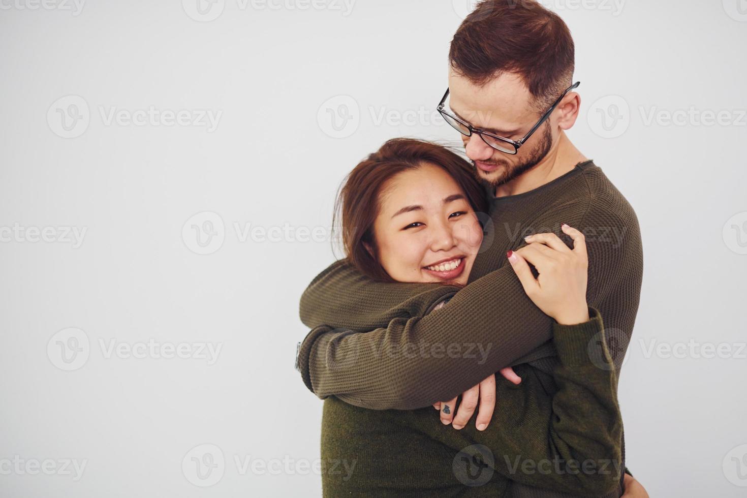 Happy multi ethnic couple in casual clothes embracing each other indoors in the studio. Caucasian guy with asian girlfriend photo