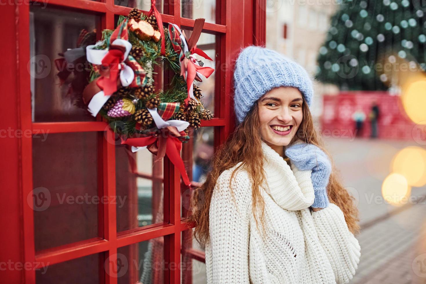 Young girl in warm clothes have a walk outdoors in the city near red phone station photo