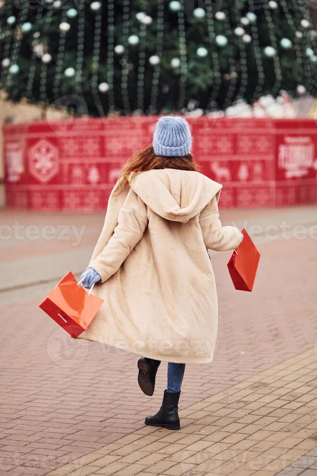 Rear view of young girl in warm clothes and with shopping bags in hands that have a walk outdoors in the city photo