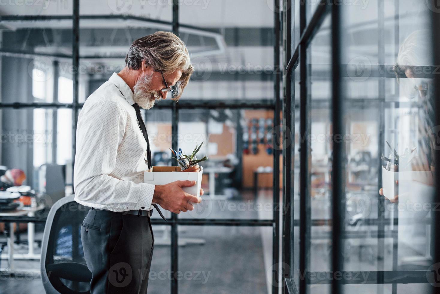 Holding box with tools. Mature businessman with grey hair and beard in formal clothes is in the office photo