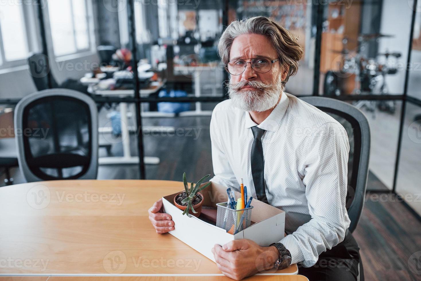 Holding box with tools. Mature businessman with grey hair and beard in formal clothes is in the office photo