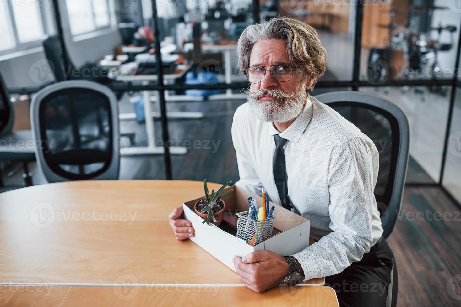 Holding box with tools. Mature businessman with grey hair and beard in formal clothes is in the office photo