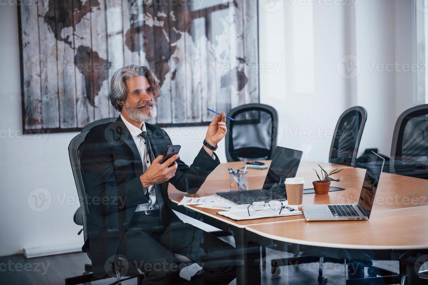 Mature businessman with grey hair and beard in formal clothes is in the office photo