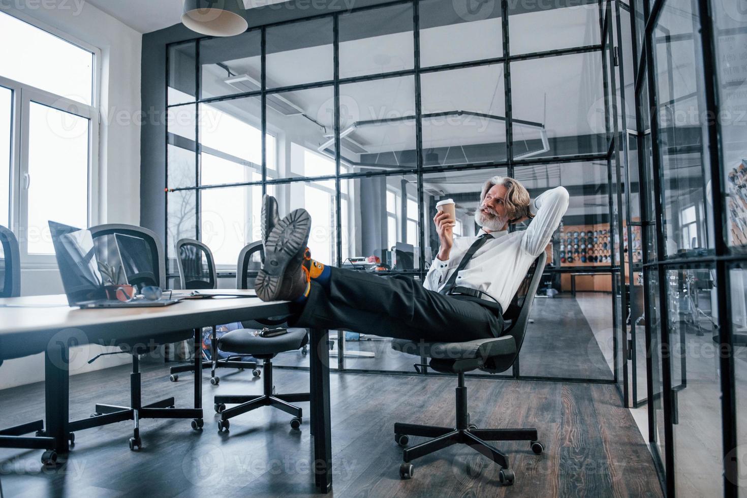 Senior businessman with grey hair and beard in formal clothes takes a break in the office photo