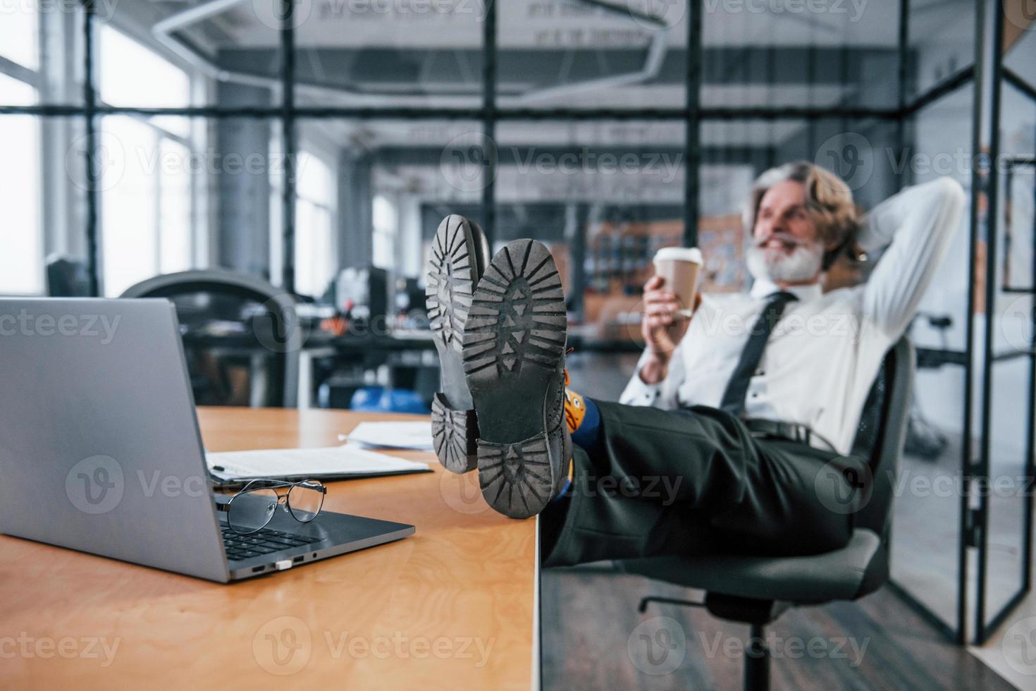 Senior businessman with grey hair and beard in formal clothes takes a break in the office photo