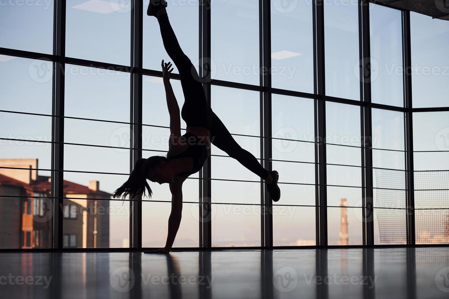 silueta de una joven deportista con ropa deportiva que hace trucos acrobáticos en el gimnasio foto