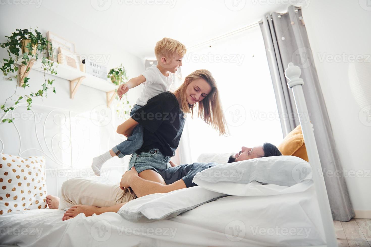 Young married couple with their young son lying down on bed and have fun together in bedroom at daytime photo