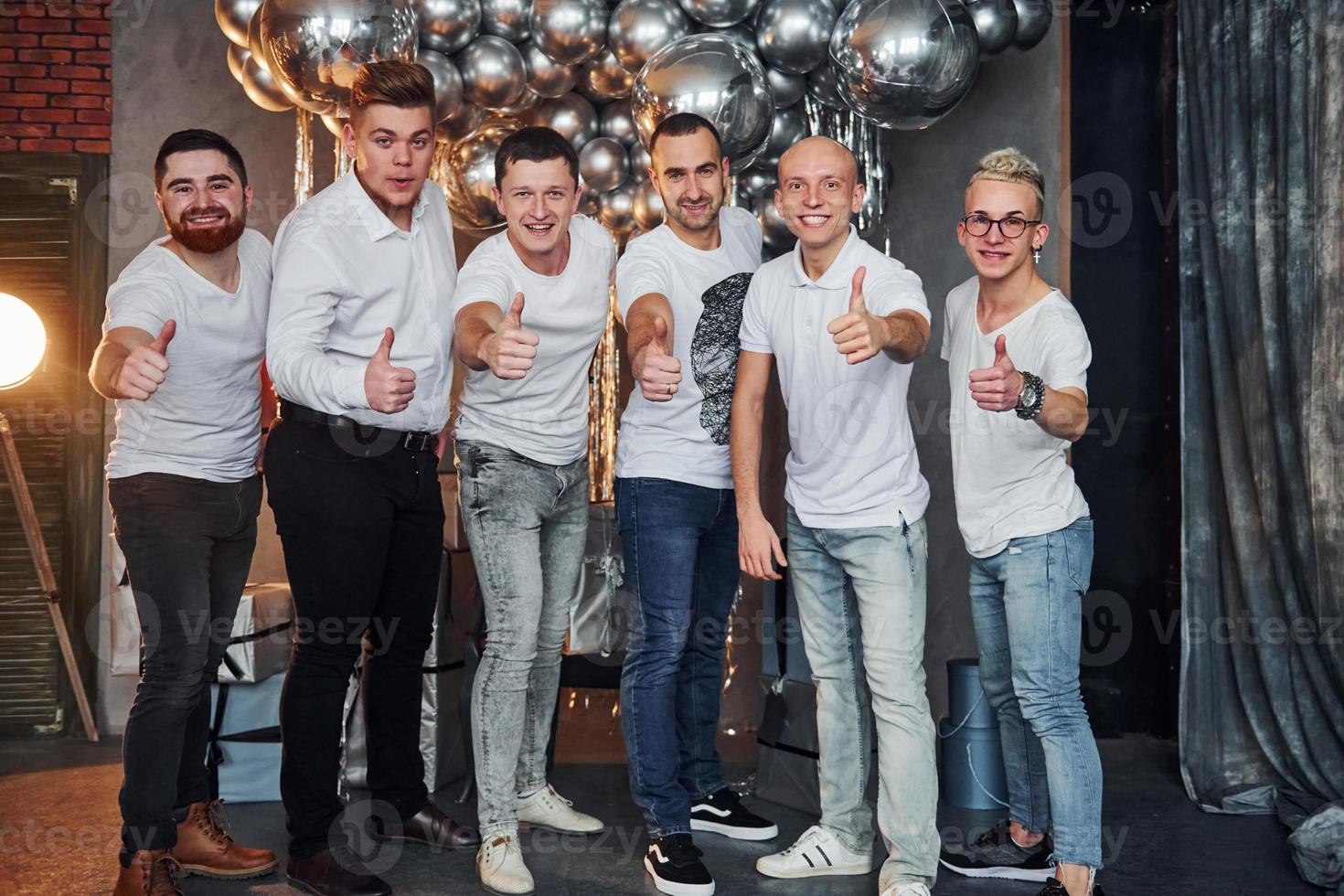 grupo de hombres alegres parados juntos en una habitación decorada con navidad y posando para una cámara foto