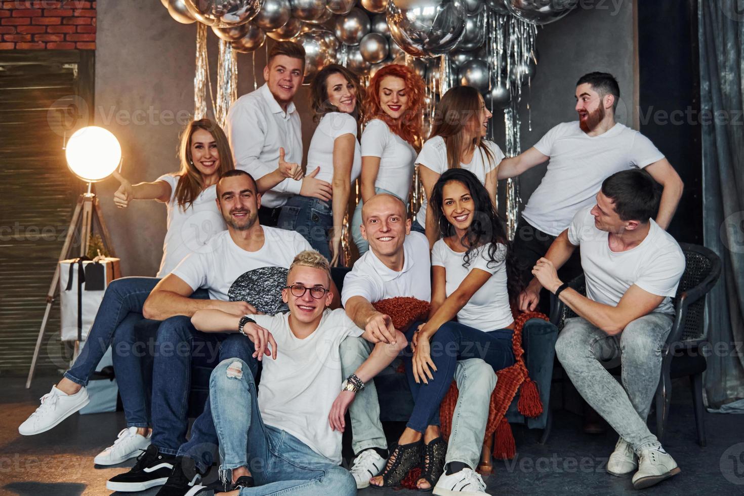 Positive young people sitting and celebrating New Year in christmas decorated room with balloons together photo