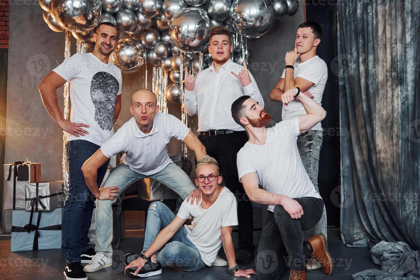 grupo de hombres alegres parados juntos en una habitación decorada con navidad y posando para una cámara foto