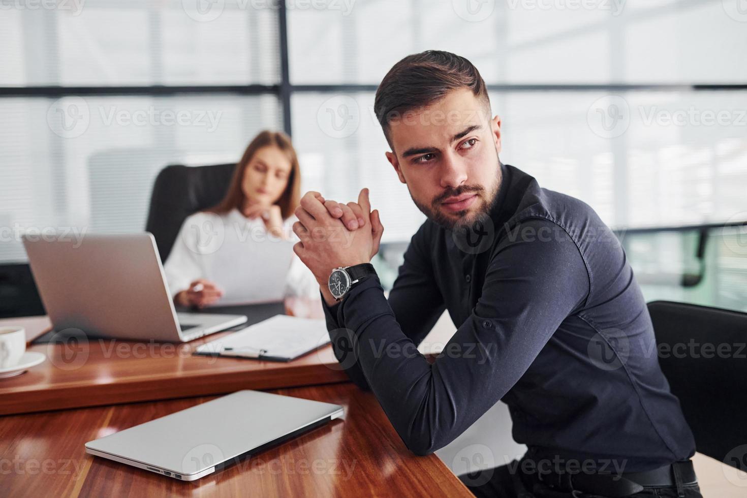 Guy sitting with documents. Woman and man in formal clothes working together indoors in the office by table photo