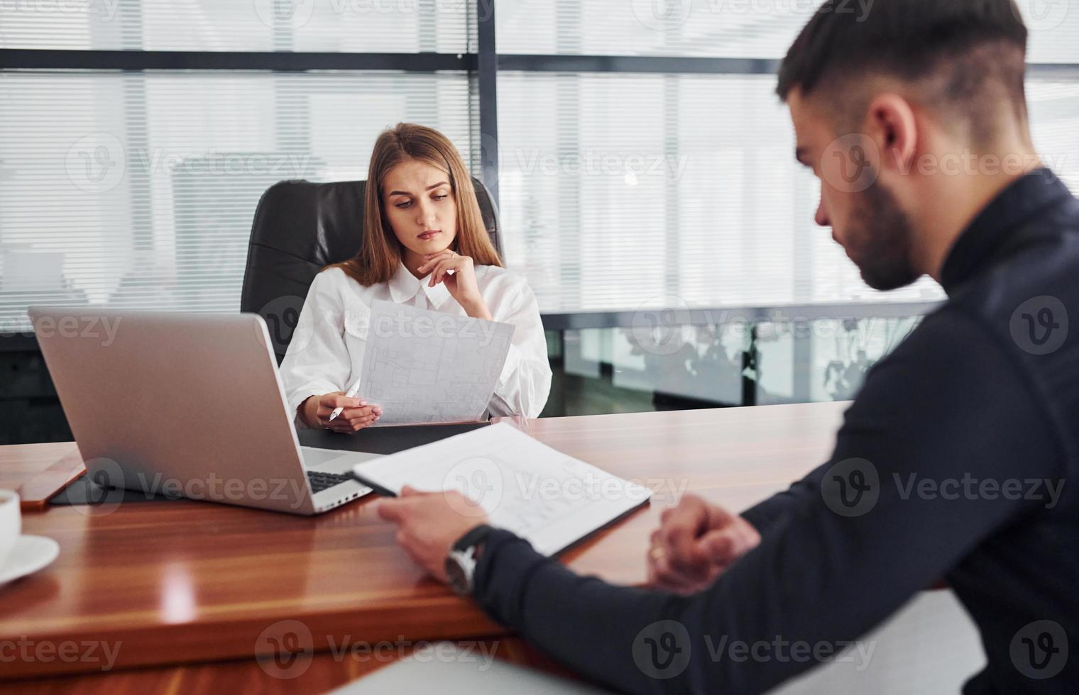 chico sentado con documentos. mujer y hombre con ropa formal trabajando juntos en el interior de la oficina junto a la mesa foto