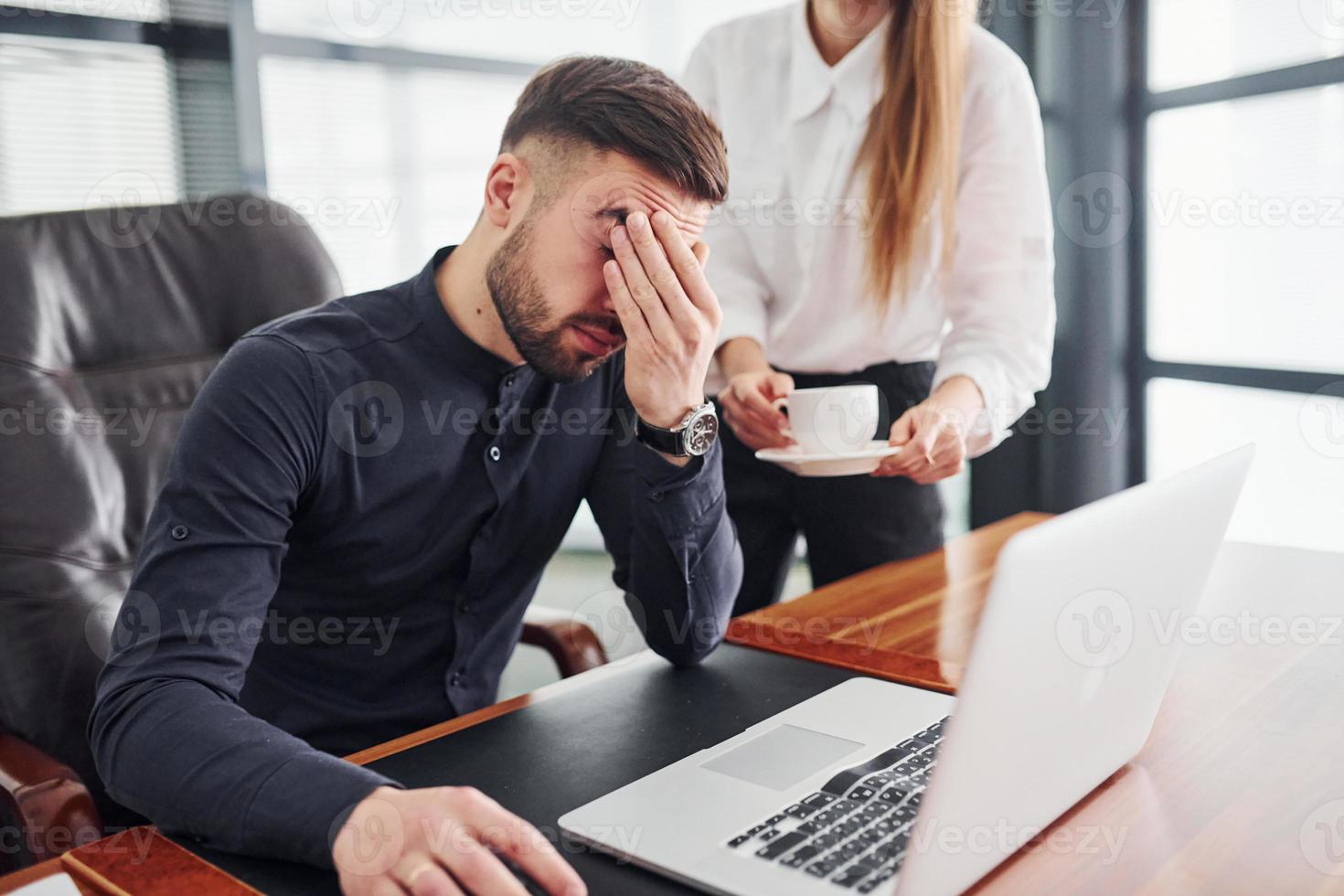 Guy feels bad. Woman and man in formal clothes working together indoors in the office by table photo