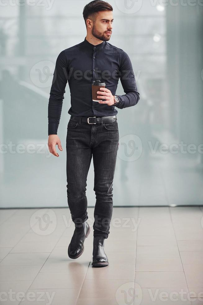 joven barbudo con ropa elegante parado en el interior contra un fondo gris foto