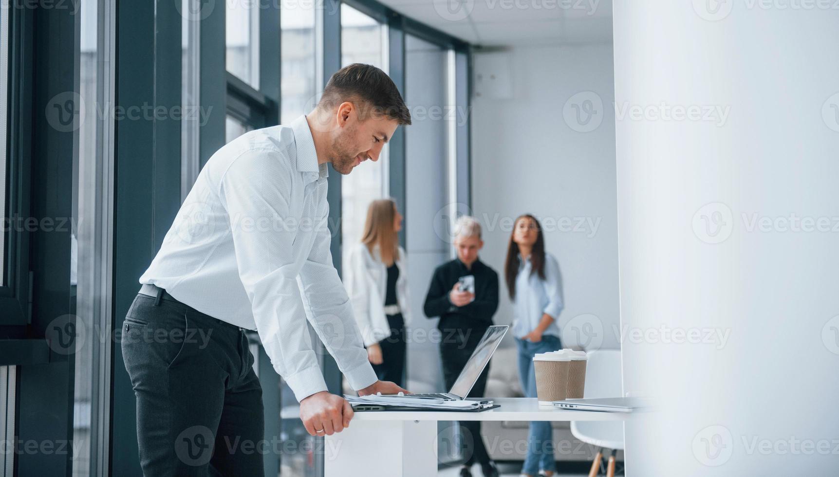 Man in formal clothes standing and reading documents in front of young successful team that working and communicating together indoors in office photo