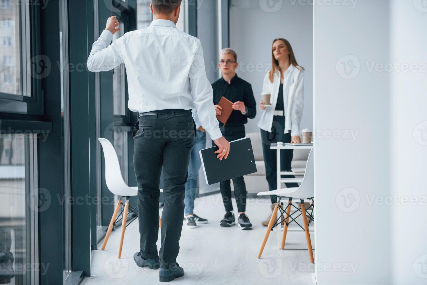 Man in formal clothes walking and talking. Group of young successful team that working and communicating together indoors in office photo