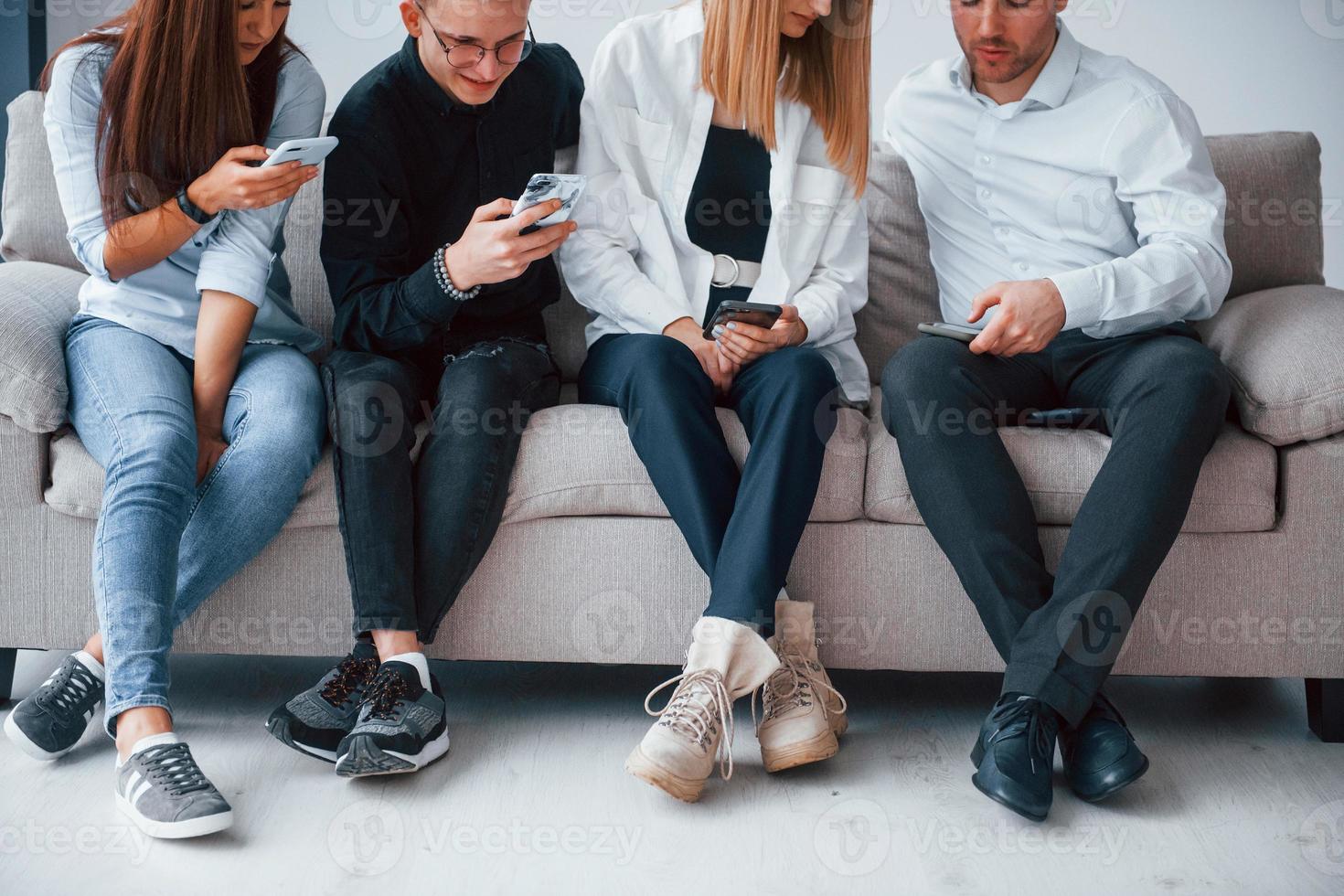 Group of friends sitting on the sofa with phones together photo