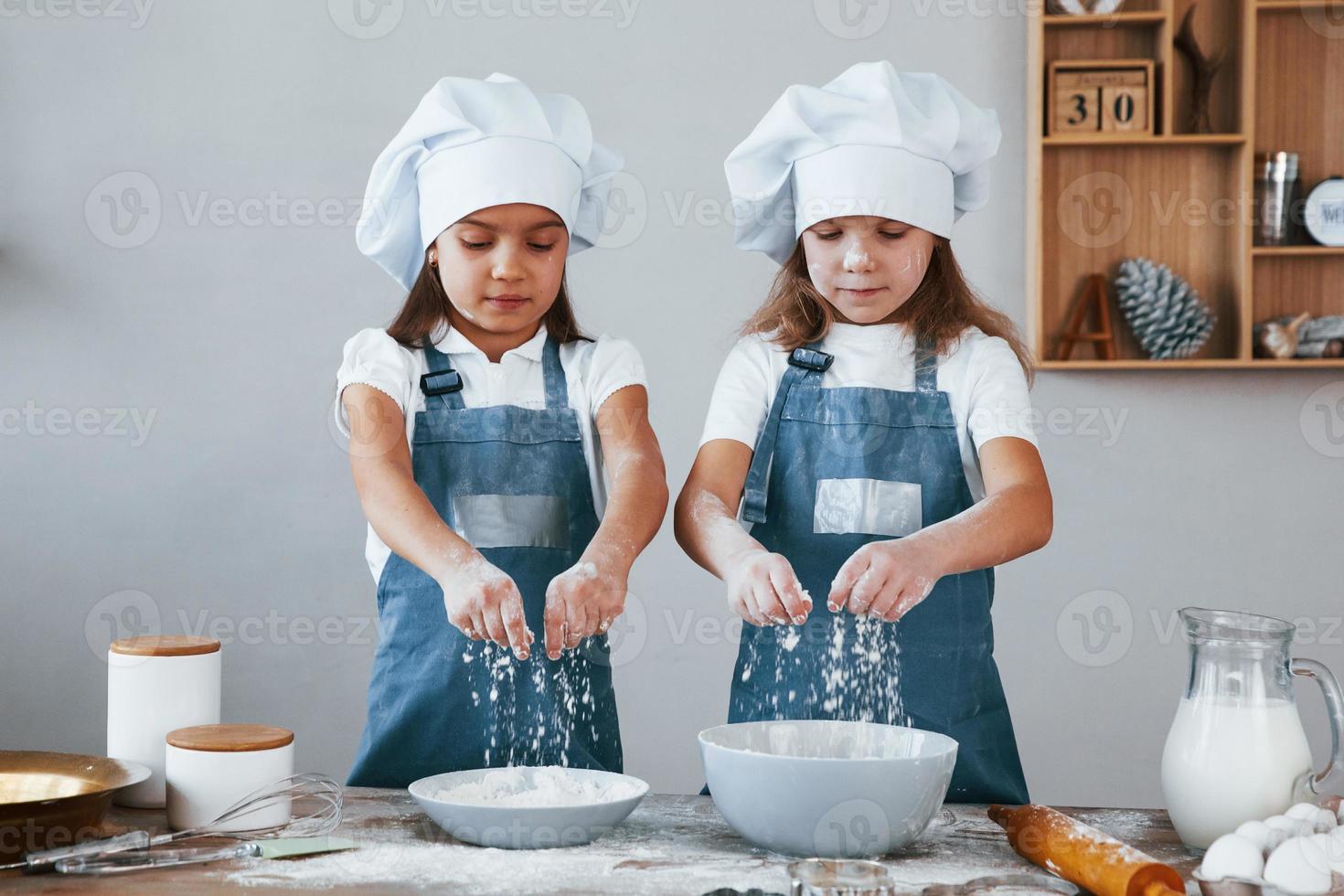 dos niñas con uniforme de chef azul trabajando con harina en la cocina foto