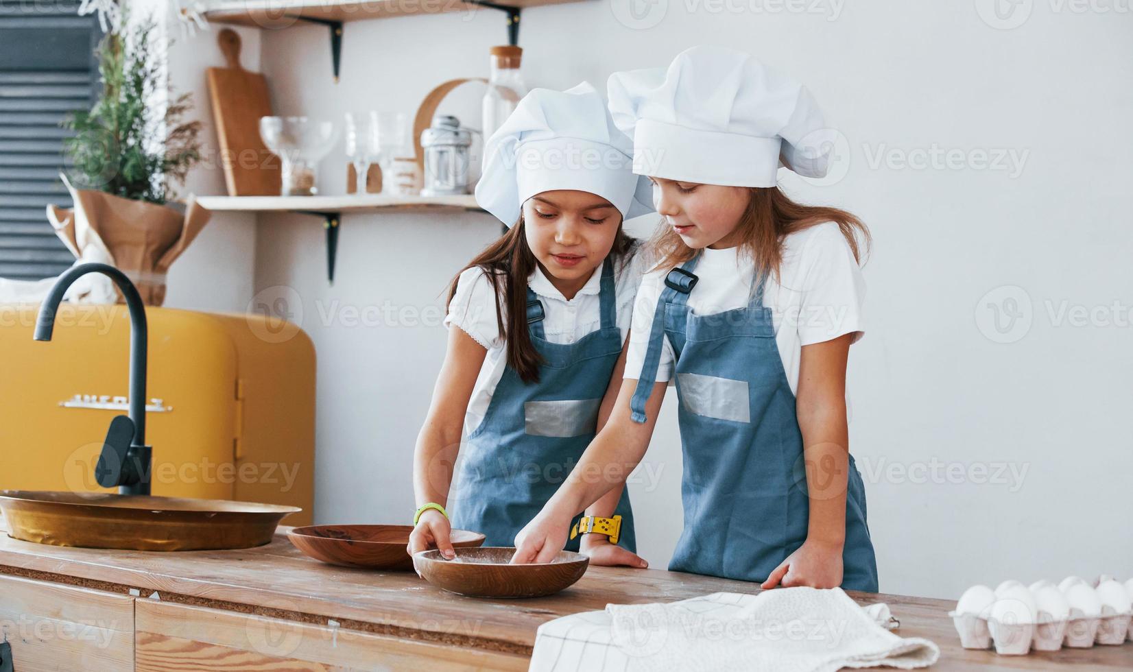 dos niñas con uniforme de chef azul trabajando con harina en la cocina foto