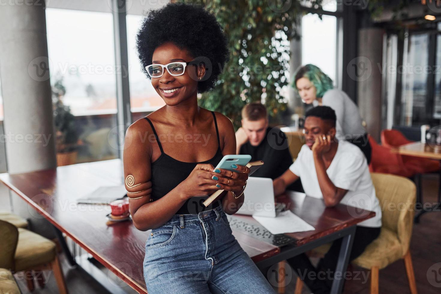 mujer negra parada frente a un grupo de personas multiétnicas con una chica alternativa con cabello verde está trabajando junto a la mesa en el interior foto