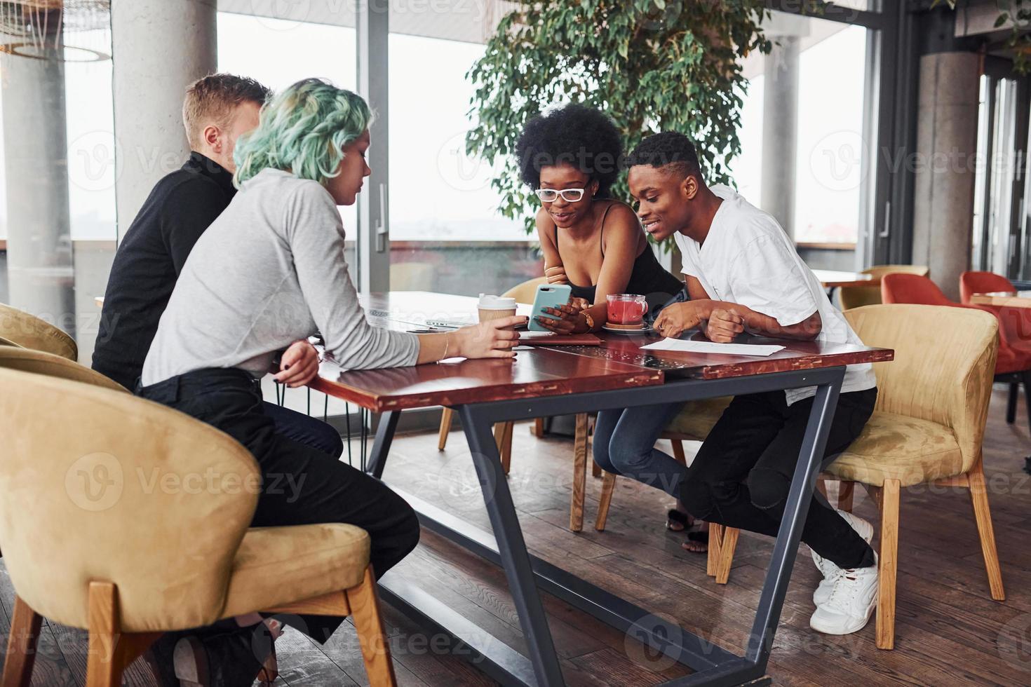 Group of multi ethnic people with alternative girl with green hair is working together by the table indoors photo