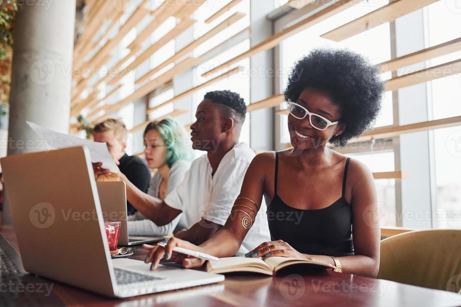 Black woman sitting in front of group of multi ethnic people with alternative girl with green hair is working together by the table indoors photo