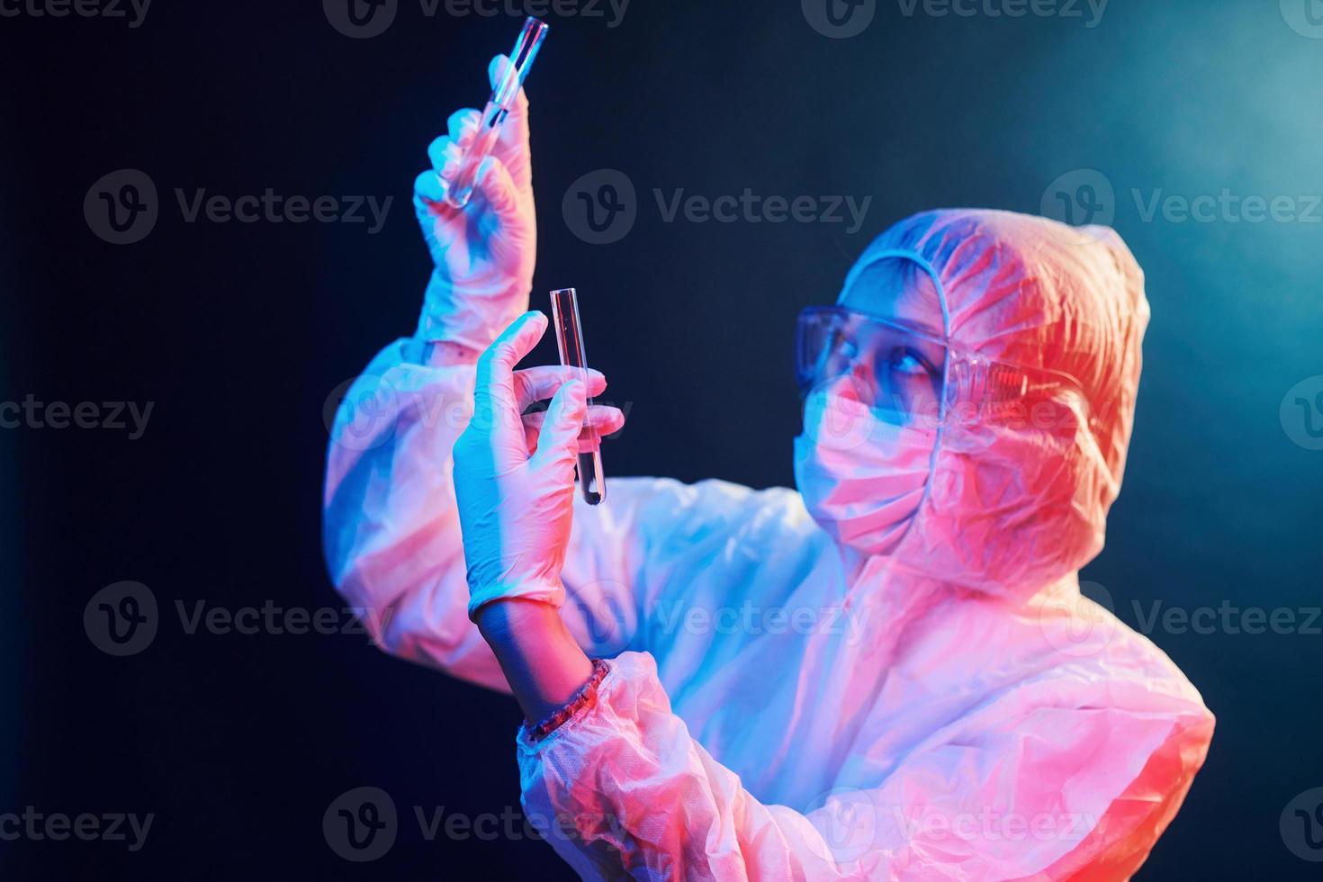 Nurse in mask and white uniform standing in neon lighted room and holding tubes with samples photo