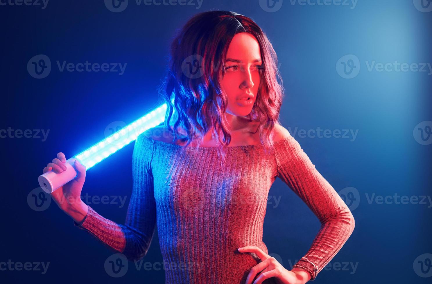 retrato de una joven con el pelo rizado que sostiene palos de luz en neón rojo y azul en el estudio foto