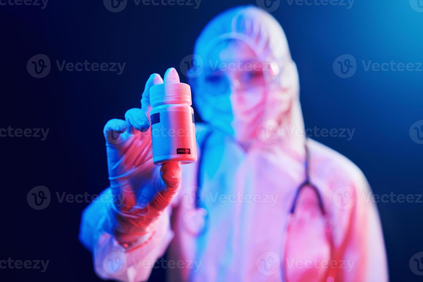 Holding cure pills for coronavirus. Nurse in mask and white uniform standing in neon lighted room photo