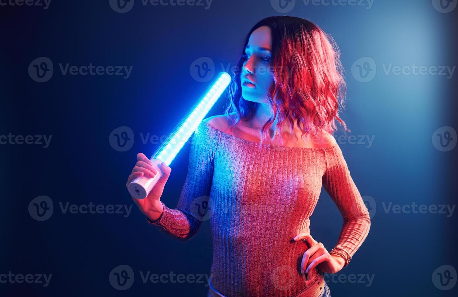 retrato de una joven con el pelo rizado que sostiene palos de luz en neón rojo y azul en el estudio foto