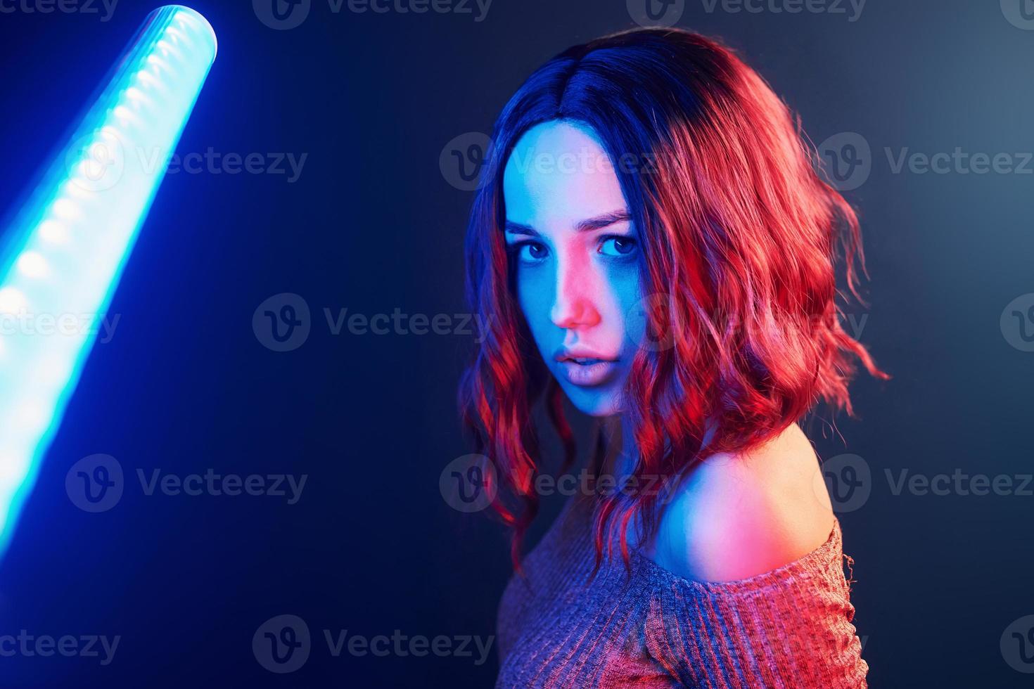 Portrait of young girl with curly hair that holds lighting sticks in red and blue neon in studio photo