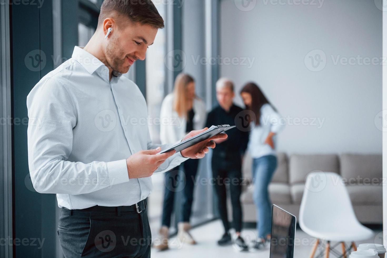 Man in formal clothes standing with documents in front of young successful team that working and communicating together indoors in office photo