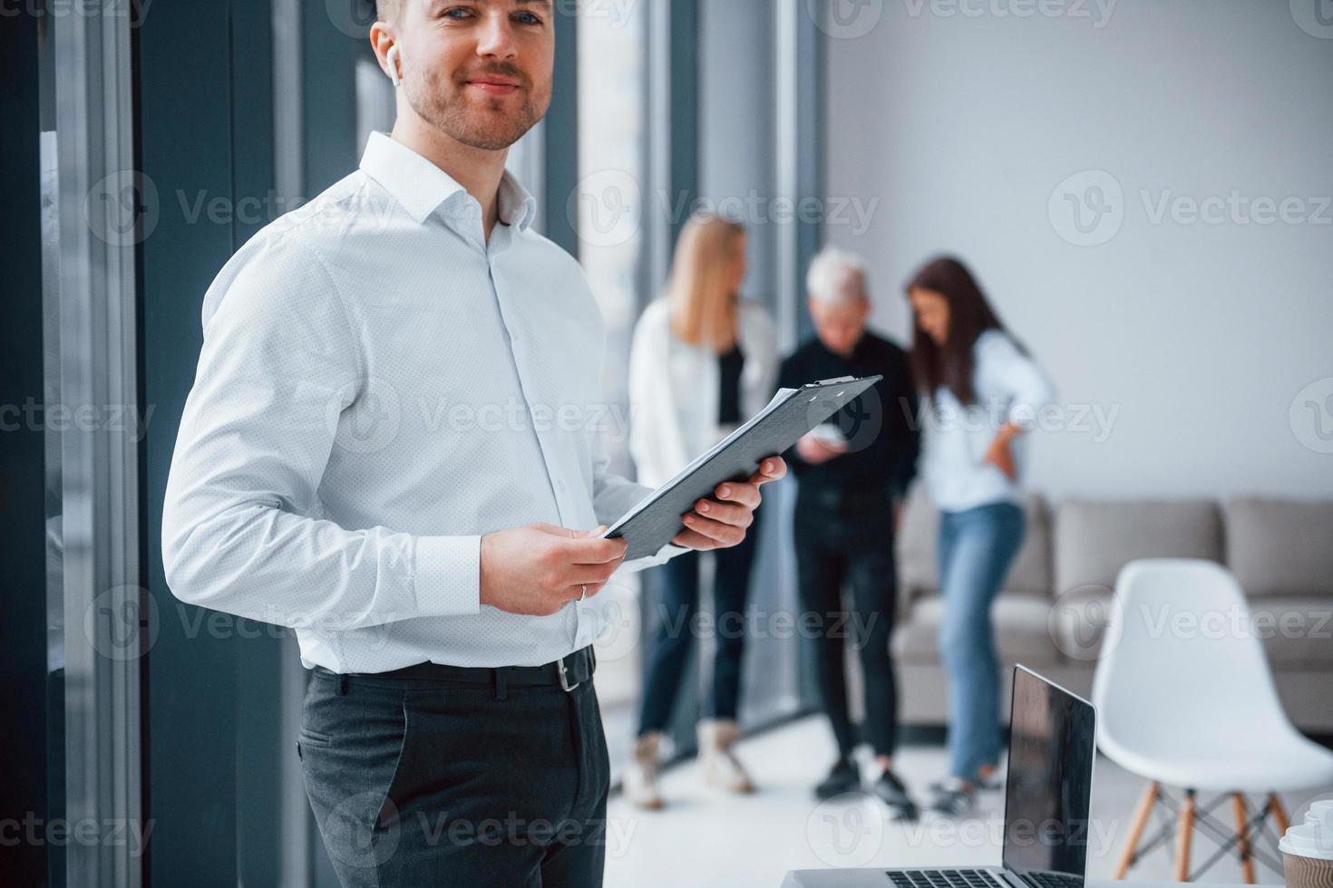 Man in formal clothes standing with documents in front of young successful team that working and communicating together indoors in office photo