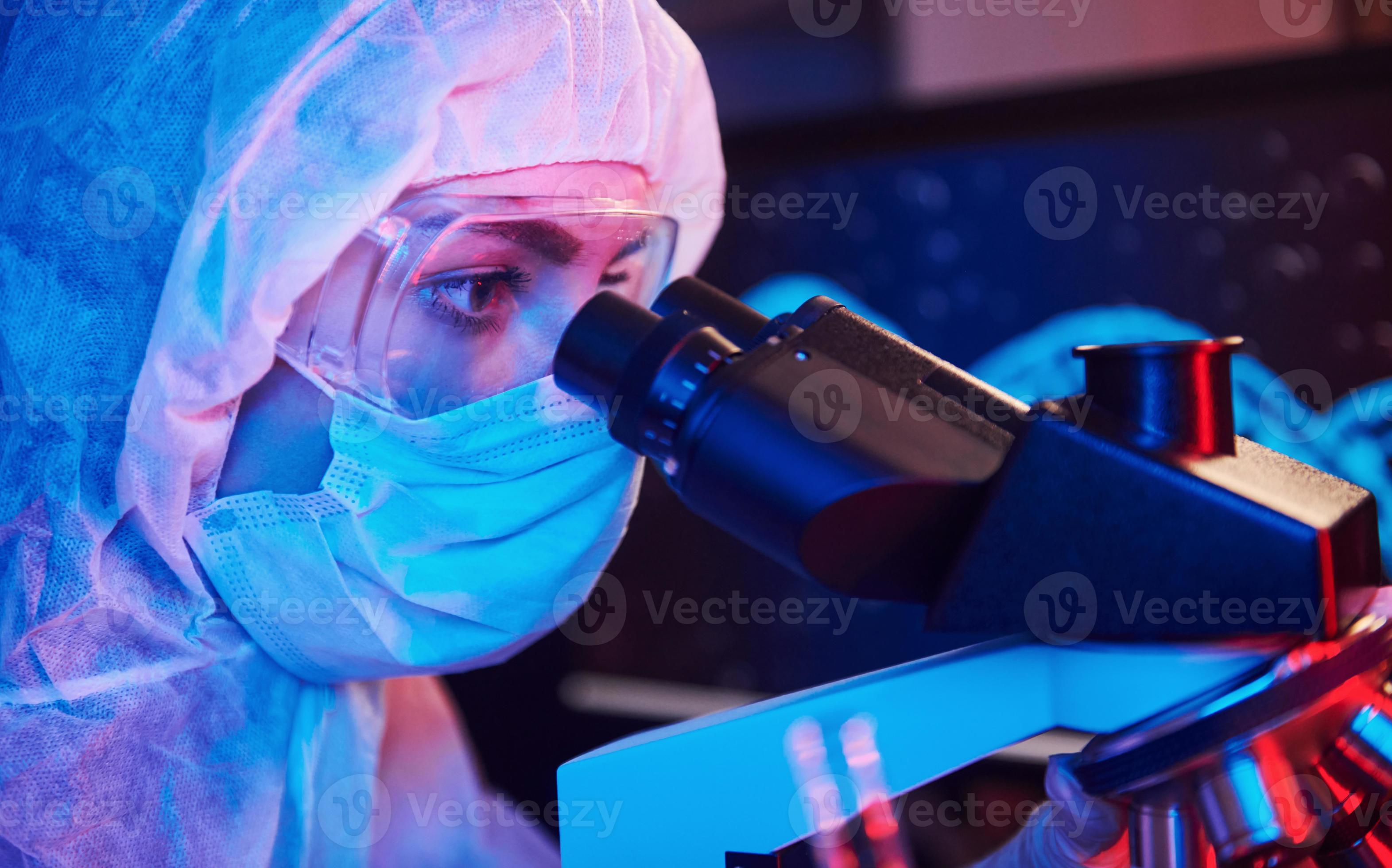 Nurse in mask and white uniform sitting in neon lighted laboratory with