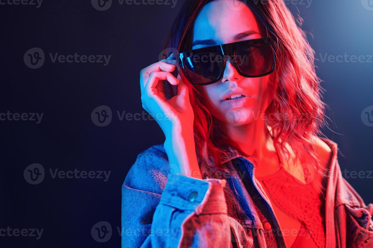Portrait of young girl in sunglasses in red and blue neon in studio