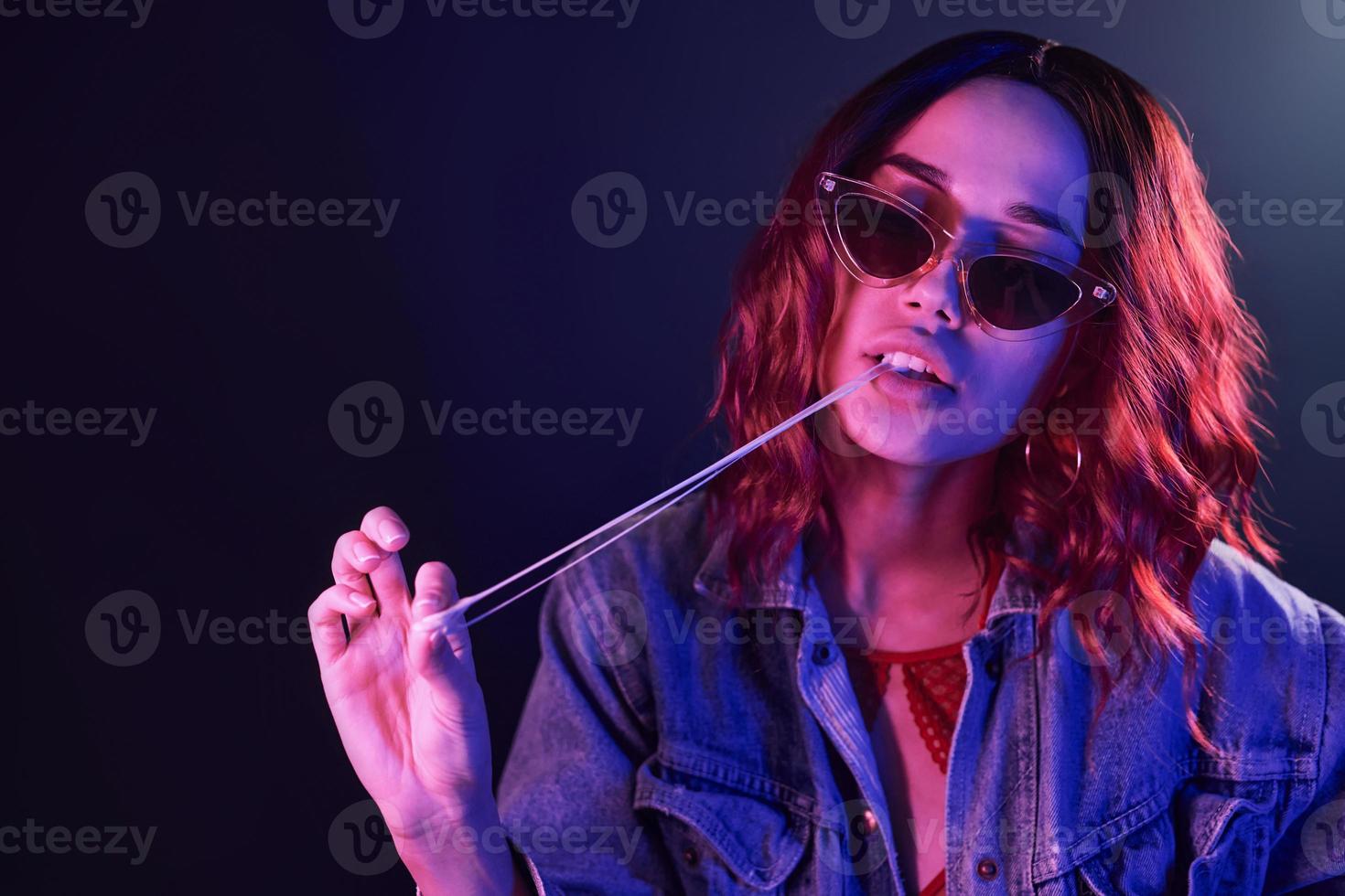 retrato de una joven con gafas con chicle en neón rojo y azul en el estudio foto