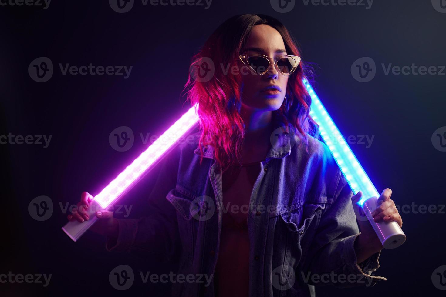 Portrait of young girl in glasses holding light sticks in red and blue neon in studio photo