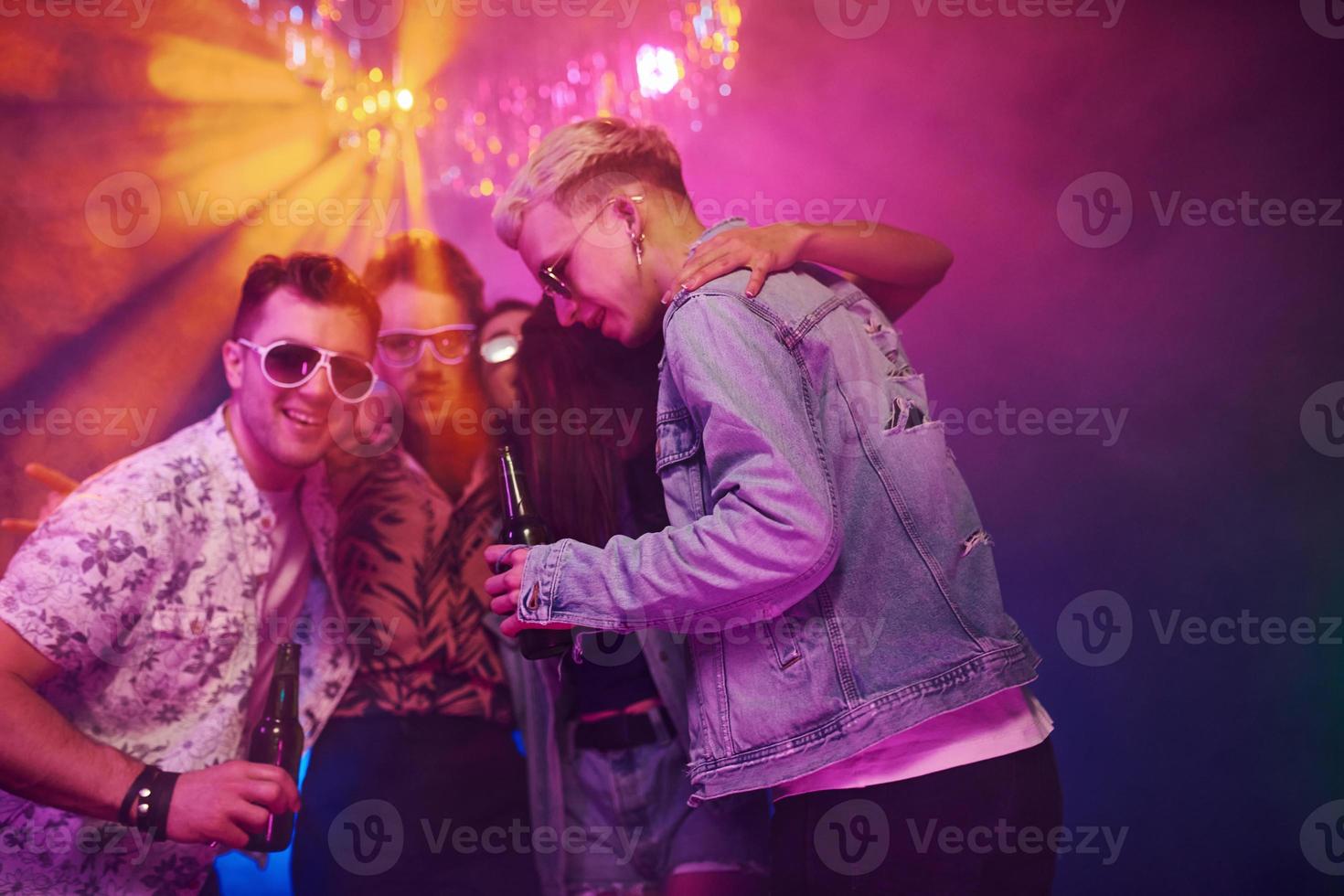 con botellas de cerveza en las manos. los jóvenes se divierten en el club nocturno con luces láser de colores foto