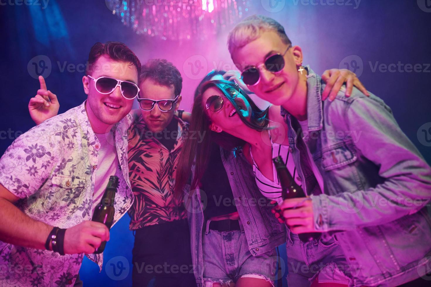 With bottles of beer in hands. Young people is having fun in night club with colorful laser lights photo