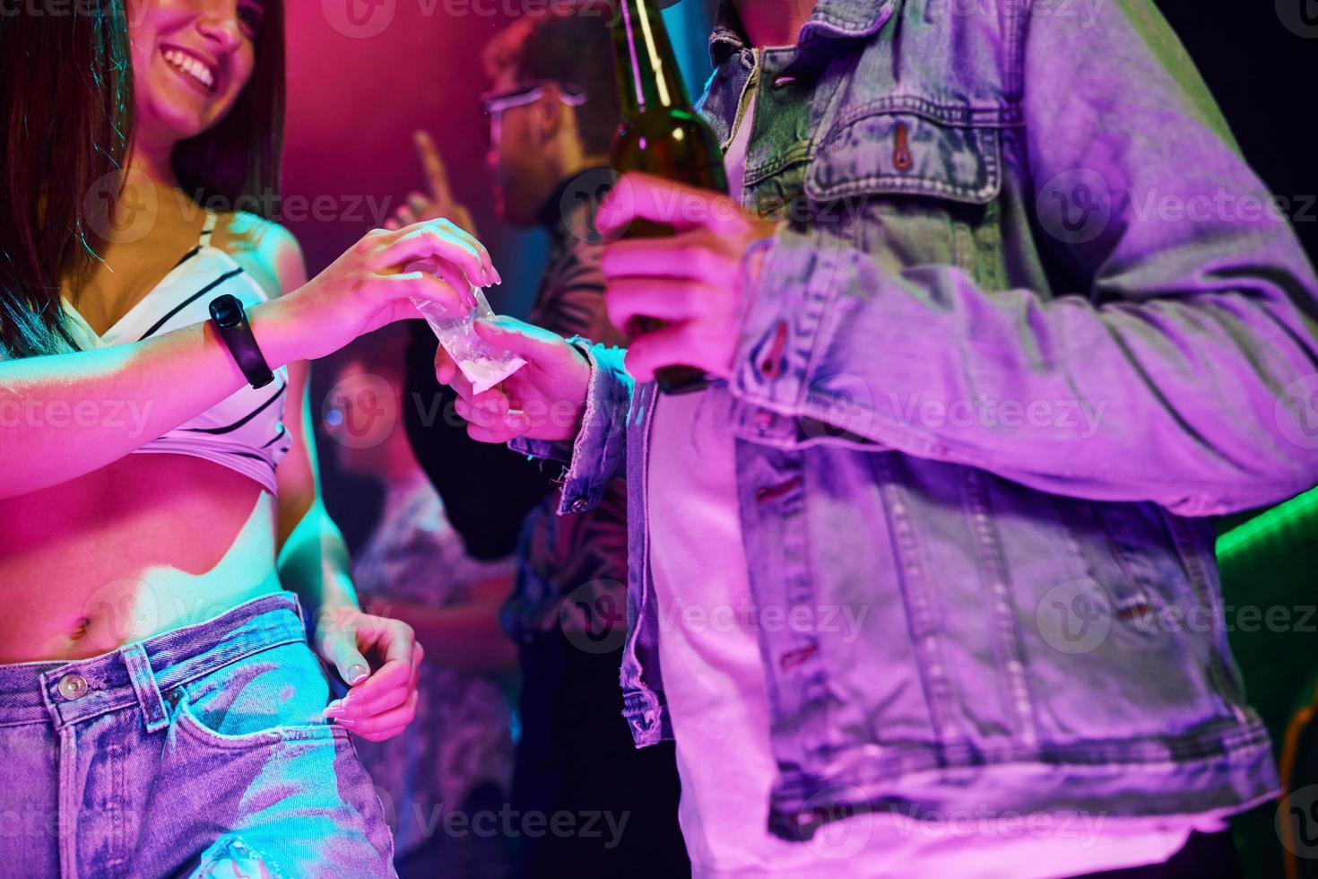 With bottles of beer in hands. Young people is having fun in night club with colorful laser lights photo