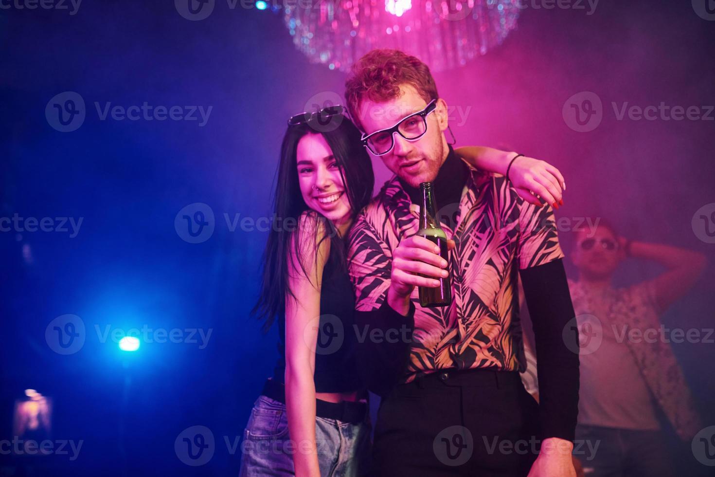 Guy in glasses drinks beer. Young people is having fun in night club with colorful laser lights photo