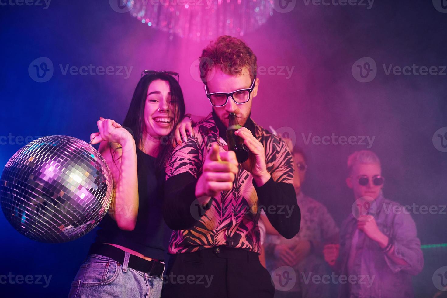 Guy in glasses drinks beer. Young people is having fun in night club with colorful laser lights photo