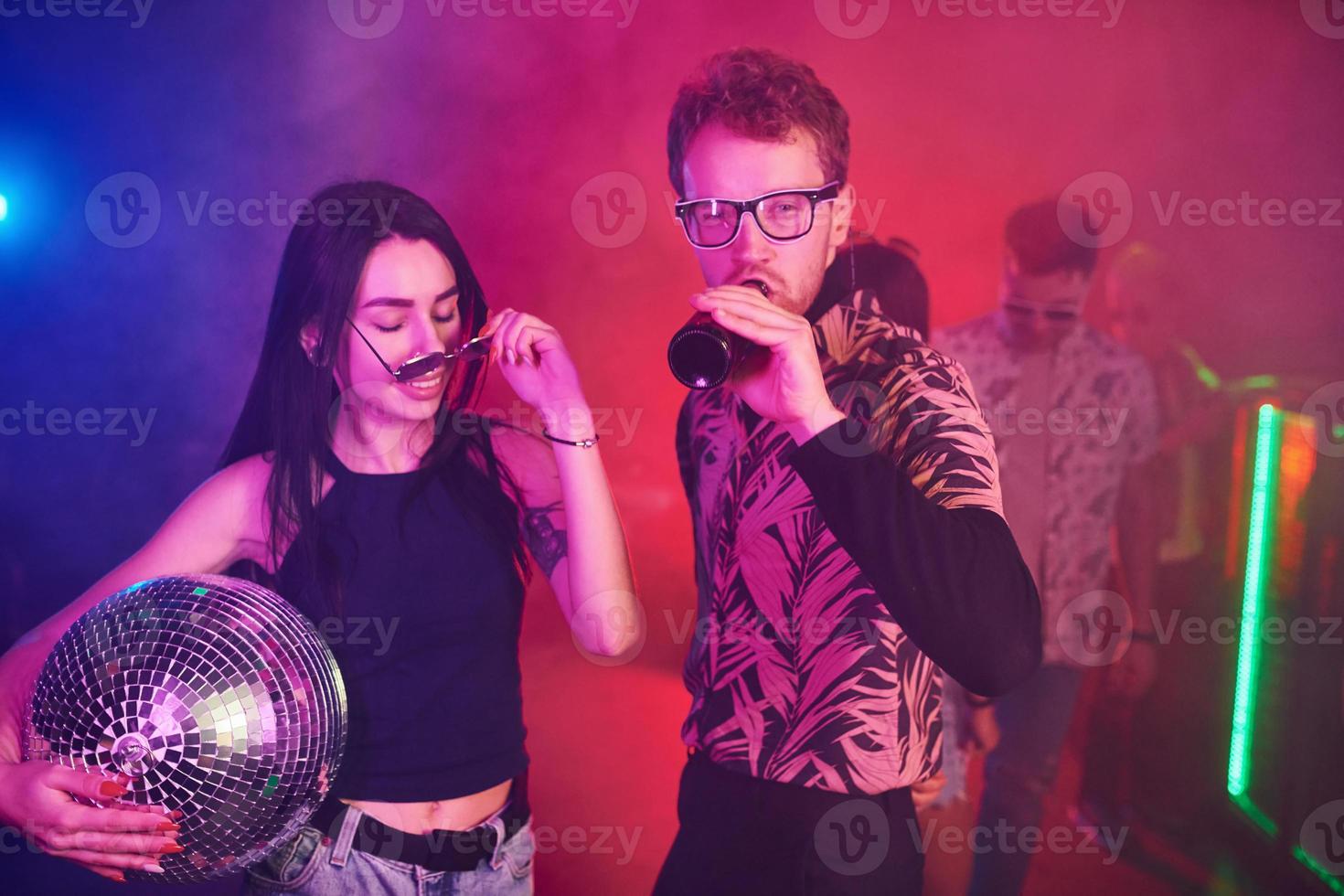 Guy in glasses drinks beer. Young people is having fun in night club with colorful laser lights photo